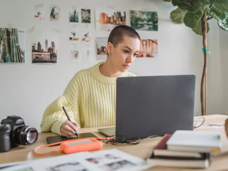 Créatrice dessinant sur une tablette graphique devant son ordinateur, un appareil photo sur le bureau.