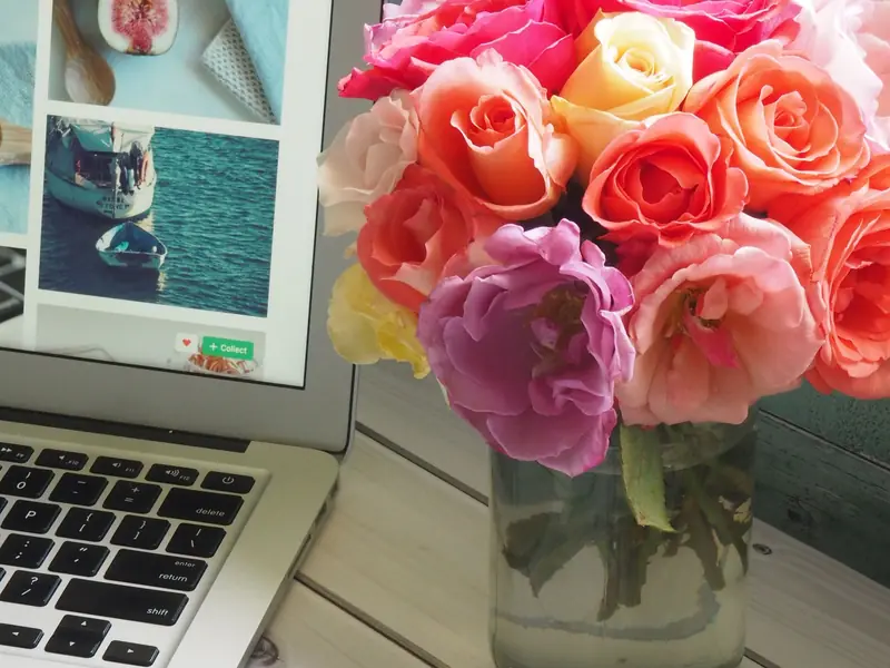 Ordinateur portable ouvert sur un bureau blanc, à côté d’un bouquet de roses et de magazines.