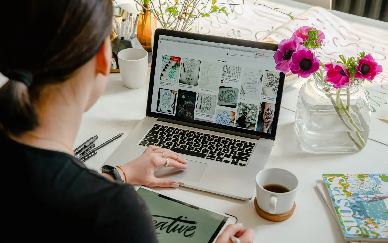 Créatrice parcourant une grille d’images sur son ordinateur portable, à côté d’un bouquet de fleurs roses.